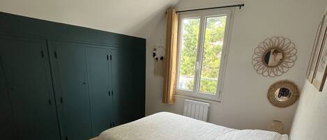 Quarto com cama, soalho de madeira, guarda-roupa, janela e objetos decorativos.