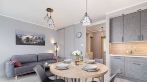 Ein modernes Wohnzimmer mit einem grauen Sofa, einem runden Esstisch mit Stühlen und einer Küchenzeile mit grauen Schränken.