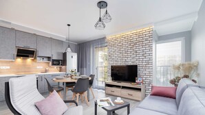 Ein modernes Wohnzimmer mit grauem Sofa, einem Esstisch und einem Fernseher vor einer Ziegelwand.