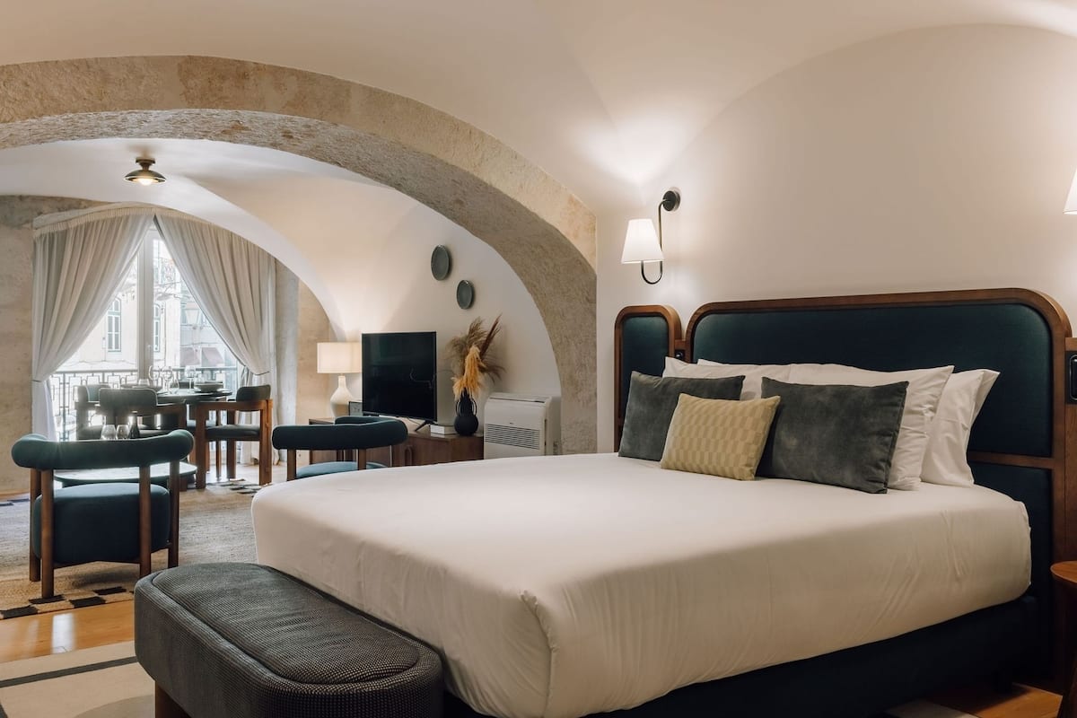 Ein Hotelzimmer mit einem großen Bett, einem Schreibtisch und Blick auf die Stadt durch ein Fenster.