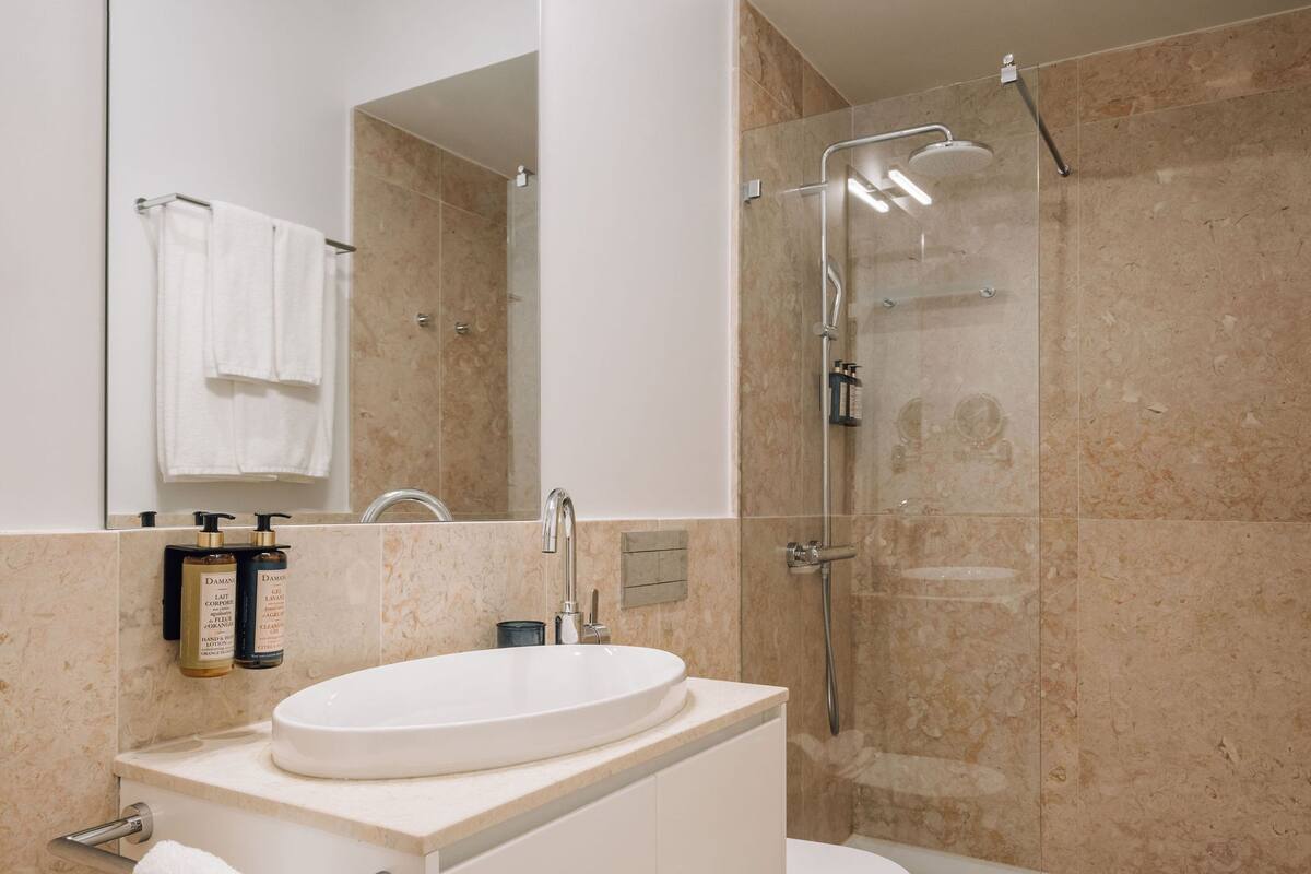 Ein modernes Badezimmer mit einem weißen Waschbecken, einer begehbaren Dusche und einem großen Spiegel.