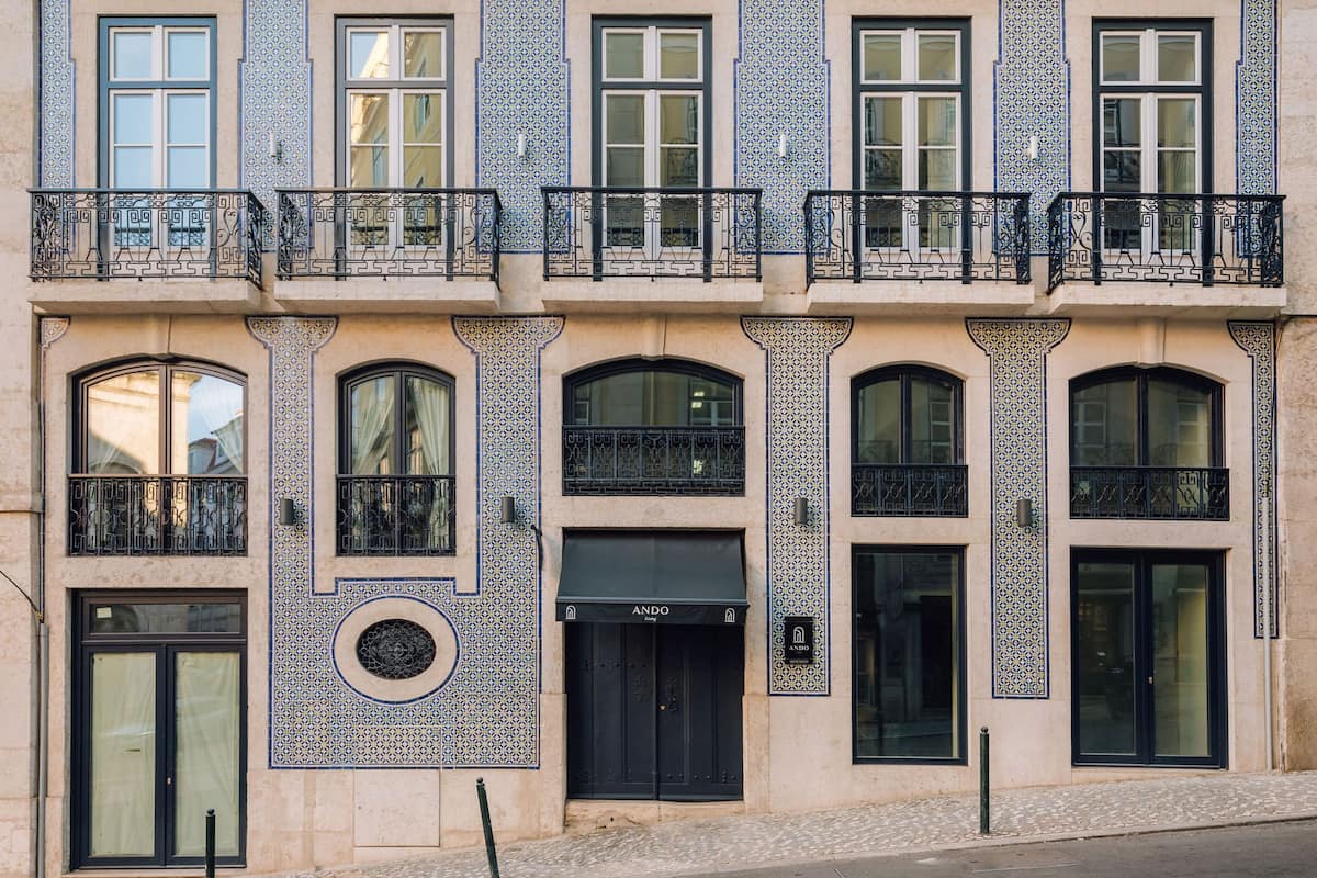 Ein Gebäude mit einer symmetrischen Fassade, das einen zentralen Eingang mit einer schwarzen Markise, mehrere Balkone mit aufwendigen Geländern und gemusterte Fliesenarbeiten an den Wänden zeigt.