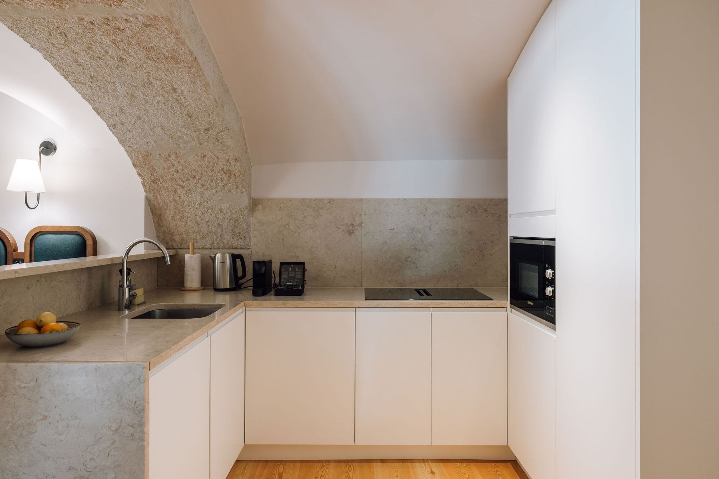 Una cucina moderna con arco in pietra, pensili bianchi, un lavello, un bollitore, una macchina da caffè e un forno a microonde.