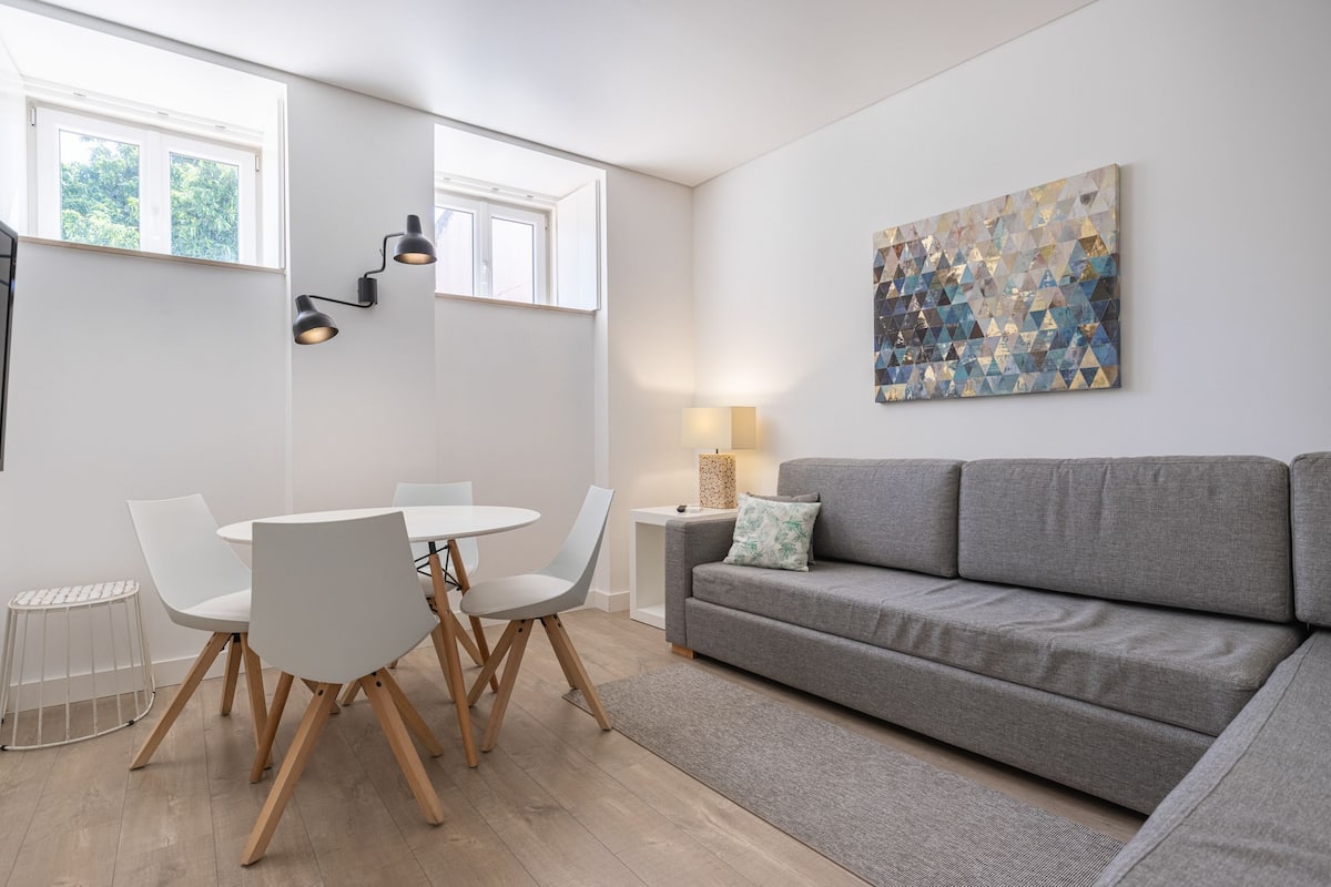 A modern living room with a grey sofa, white chairs, a round table, and a large abstract painting on the wall.