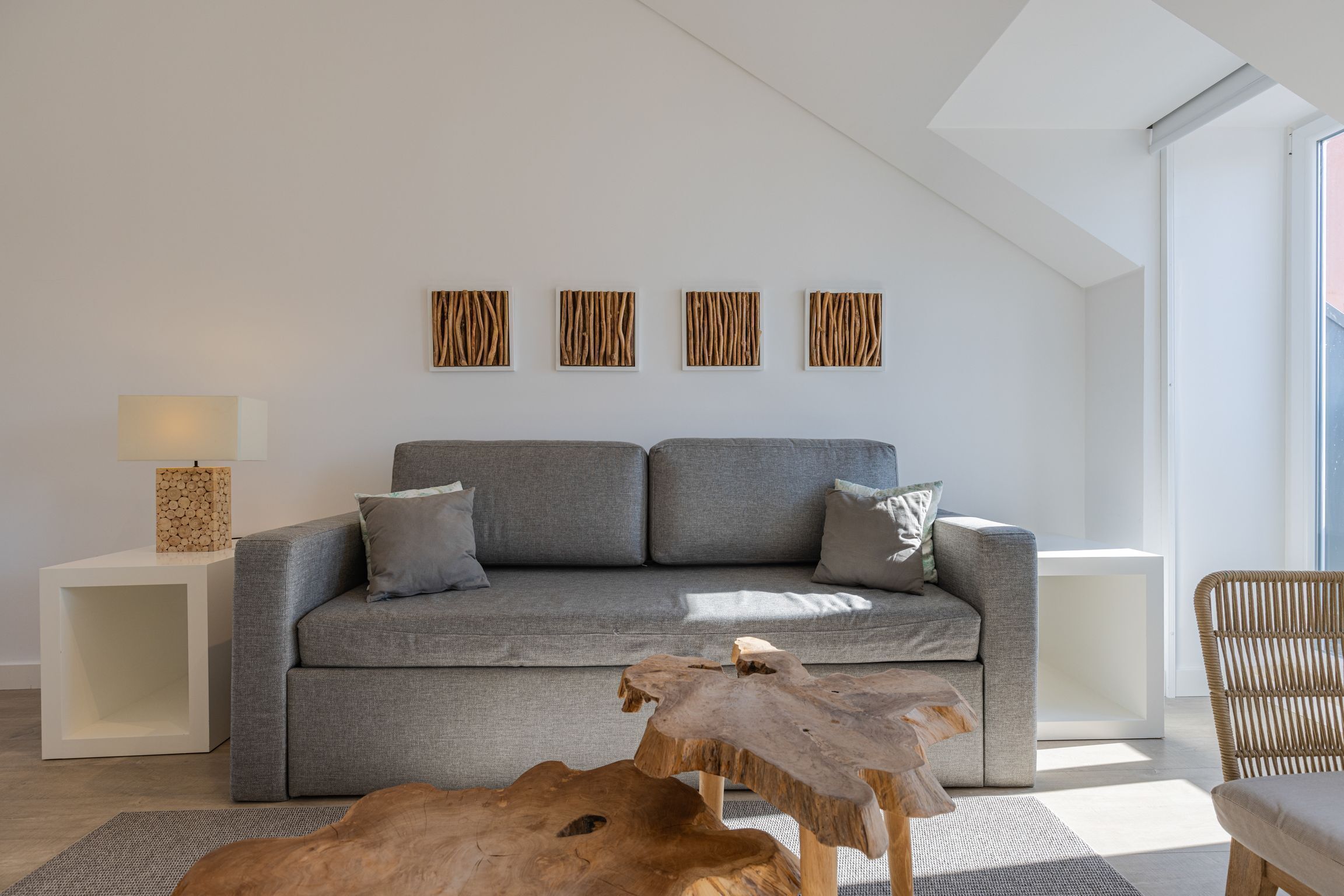 A modern living room with a grey sofa, wooden coffee table, and a large window providing natural light.