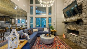 A spacious living room with a large gray sectional sofa, a round coffee table, a stone fireplace, and a television mounted on the wall.