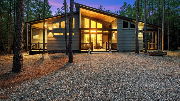A cabin with a large open porch, surrounded by trees, and a gravel driveway.
