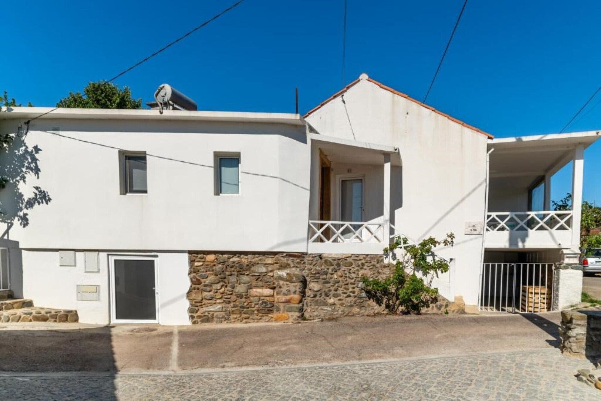 A two-story building with a stone foundation, a balcony with a white railing, and a small door.