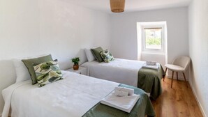 Een kamer met twee enkele bedden, een kleine tafel met een stoel, een raam met uitzicht en een hanglamp.