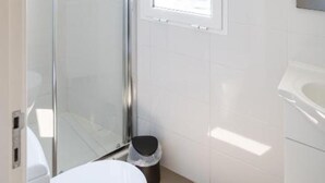 Een moderne badkamer met een douchecabine van glas, een witte wastafel en een raam voor natuurlijk licht.