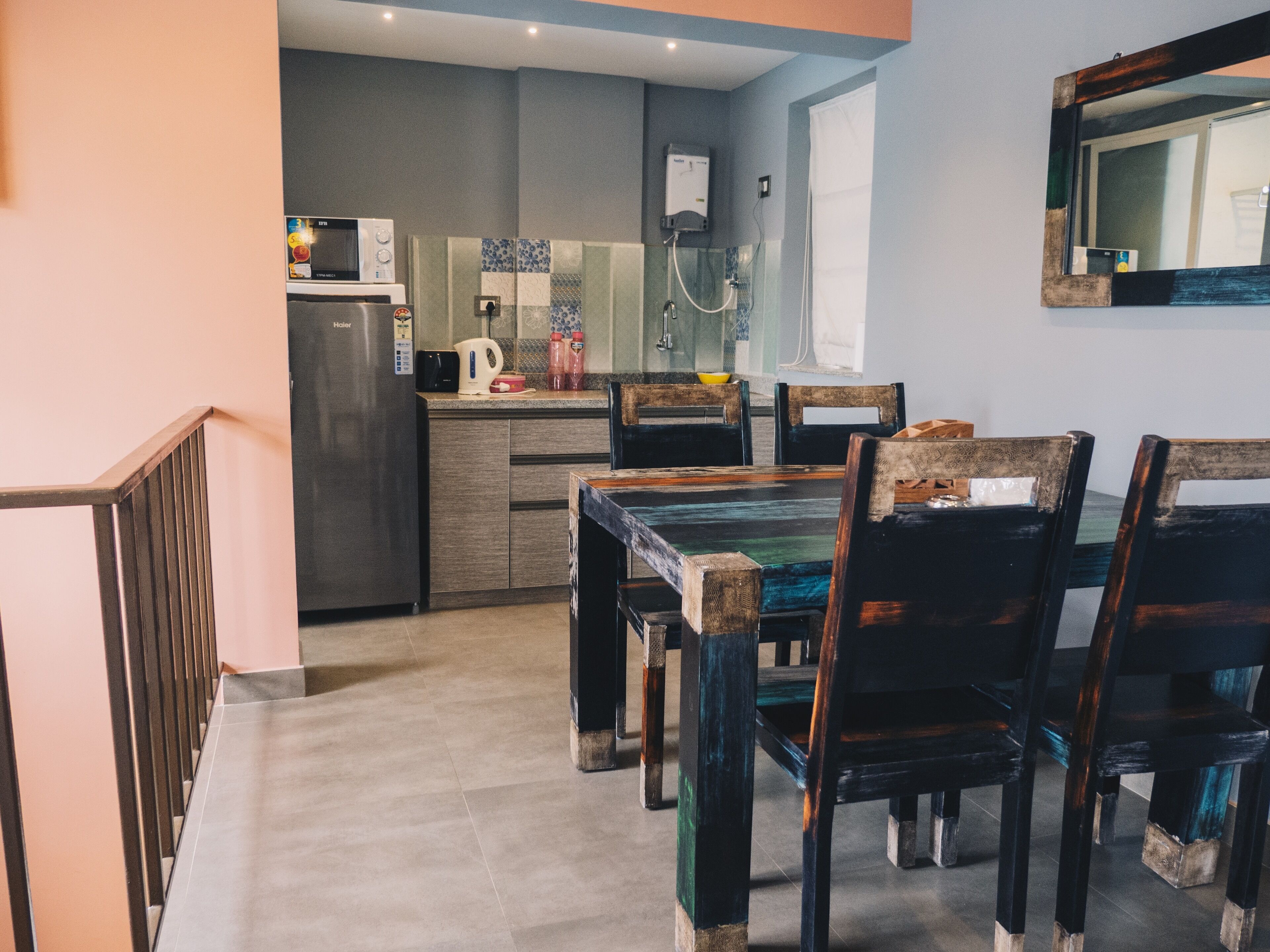 A modern kitchen with a built-in microwave, a kettle, and a coffee maker. There is a dining table with chairs and a window above it.