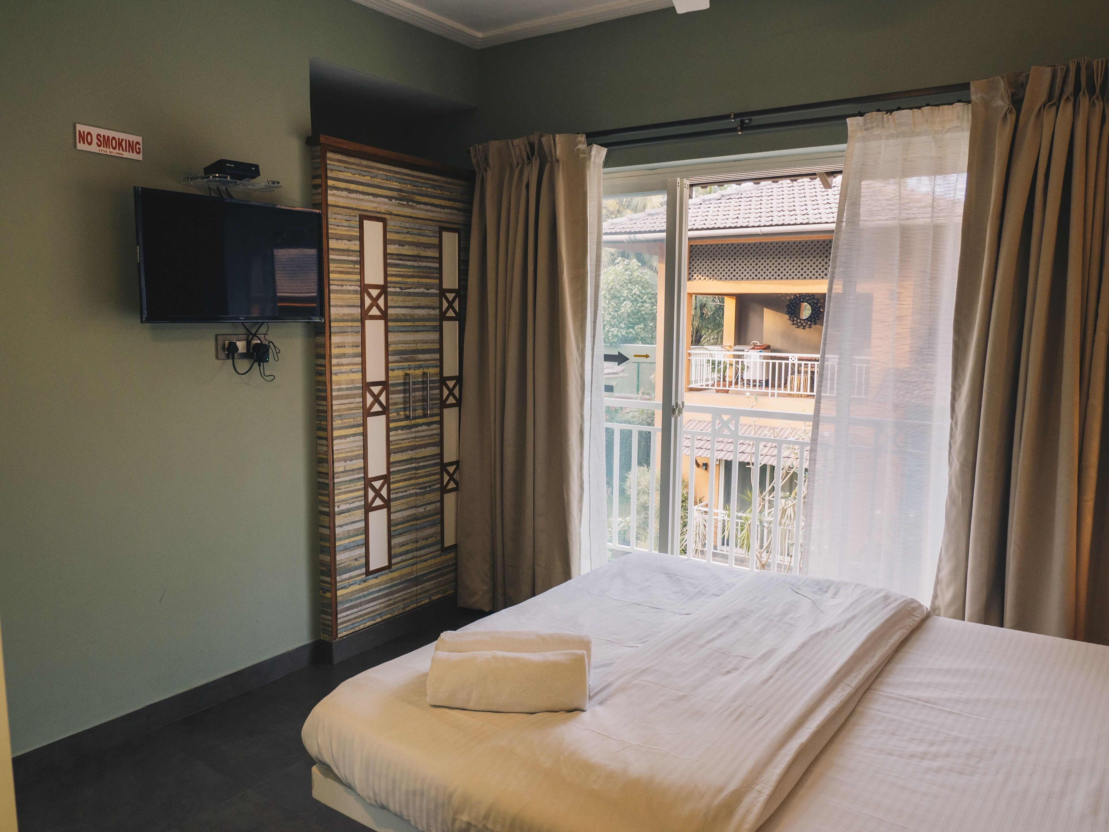 A bedroom with a bed, a TV mounted on the wall, a sliding door, and a balcony with a view of the outside.