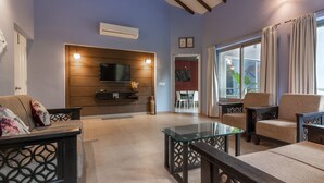 A modern living room with a flat-screen TV mounted on a wooden wall, a glass coffee table, and comfortable seating. - Luxury villa Diva Goa (Calangute)