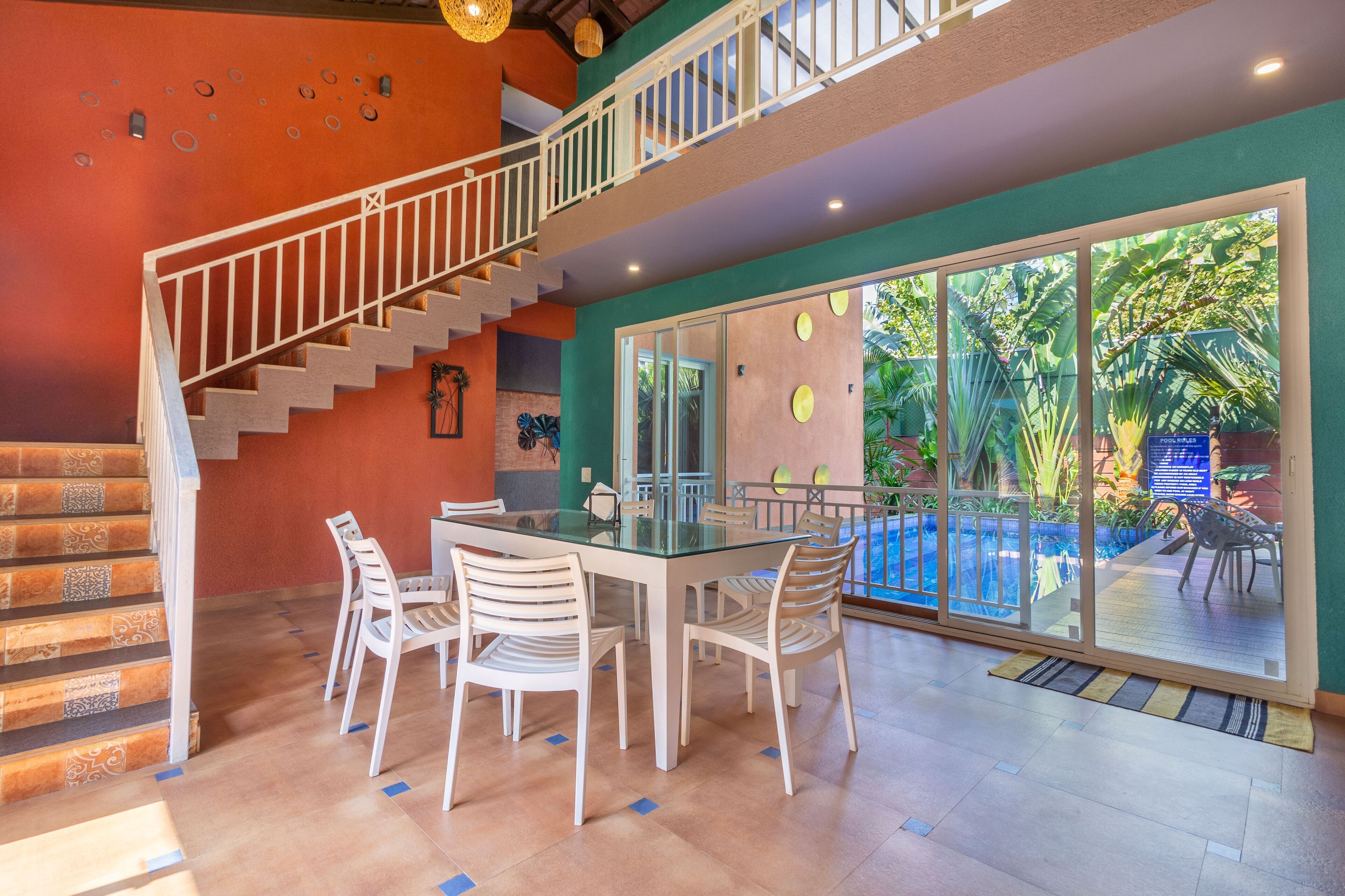 A dining area with a glass table and chairs, a staircase, and a view of a pool through large glass doors.