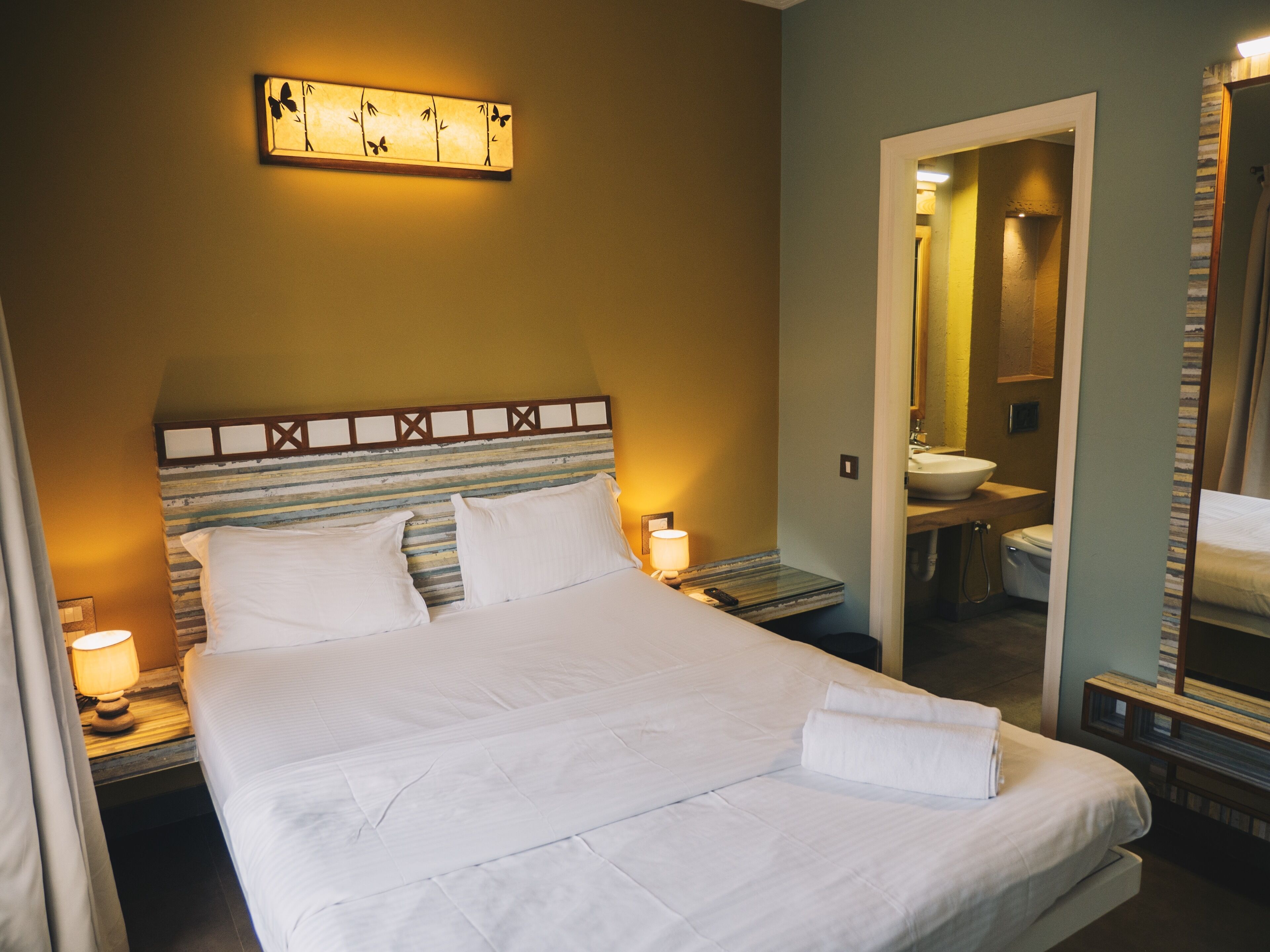 A neatly made bed with white linens, a bedside lamp, and a wall-mounted light fixture.