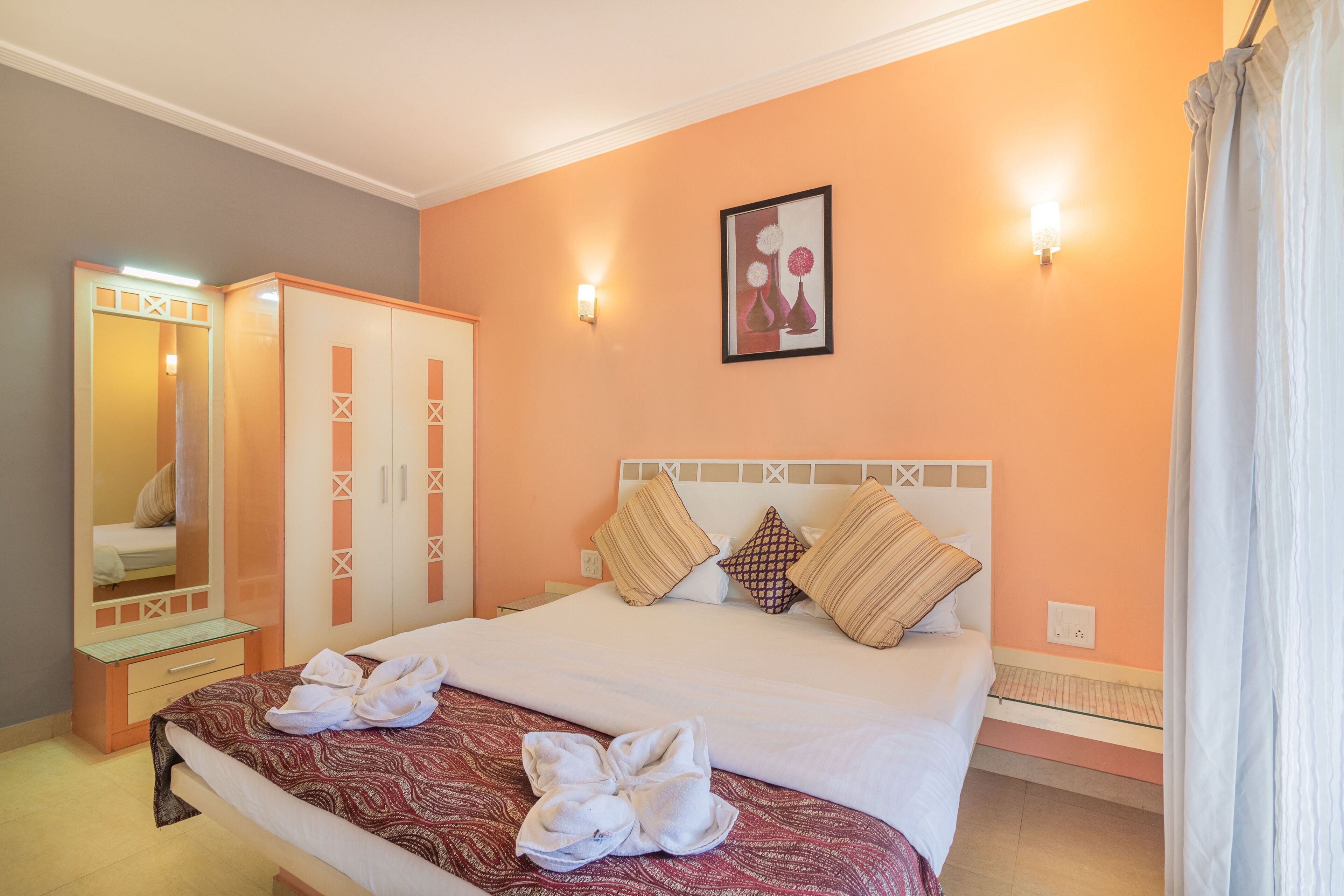 A hotel room with a bed, a wardrobe, a mirror, and a wall-mounted light fixture.