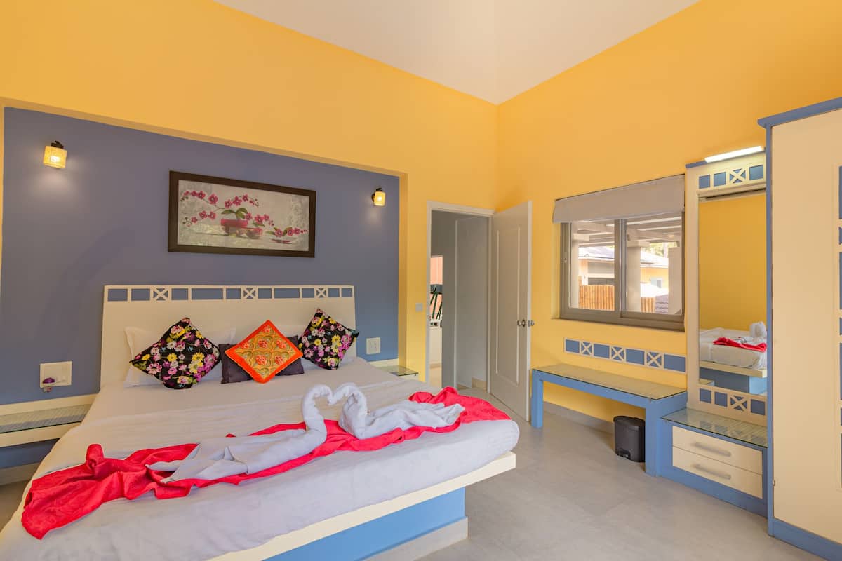 A bedroom with a bed, pillows, a bedside table, a mirror, and a door leading to another room.