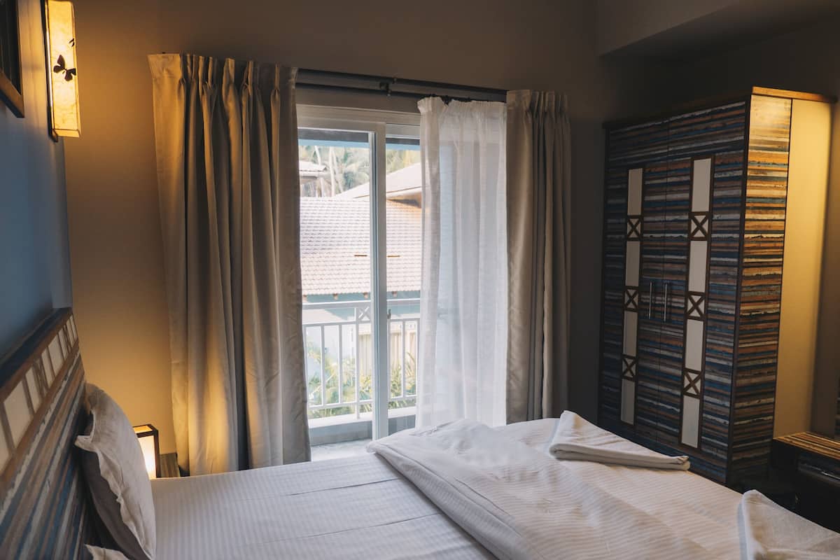 A hotel room with a bed, curtains, a view of the outside, and a wardrobe.