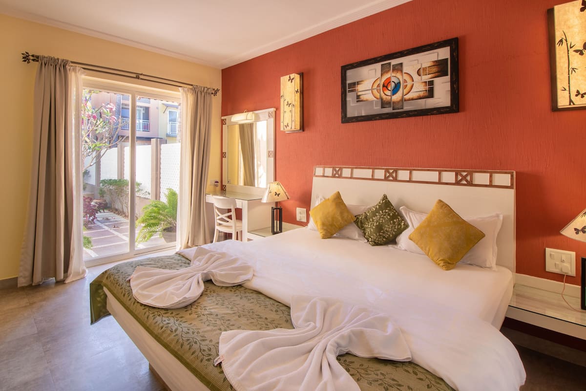 A hotel room with a bed, a desk, a chair, a window with curtains, and a painting on the wall.