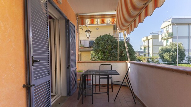 A balcony with a table and chairs, a closed door, and a view of neighboring buildings. - PRATORANIERI - GIRASOLE (Follonica)