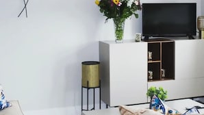 A modern living room with a flat-screen TV on a white console, a vase with flowers, and a decorative wall piece. - Enjoy the breathtaking view which you Relax at the Aran View Lodge (Doolin)