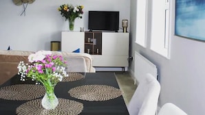 A modern living room with a sofa, a dining table with a vase of flowers, a flat-screen TV, and a large abstract painting. - Enjoy the breathtaking view which you Relax at the Aran View Lodge (Doolin)