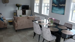 A living room with a beige sofa, a TV, and a dining table with chairs. - Enjoy the breathtaking view which you Relax at the Aran View Lodge (Doolin)