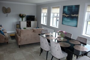 Ein Wohnzimmer mit einem beigefarbenen Sofa, einem Fernseher und einem Esstisch mit Stühlen.