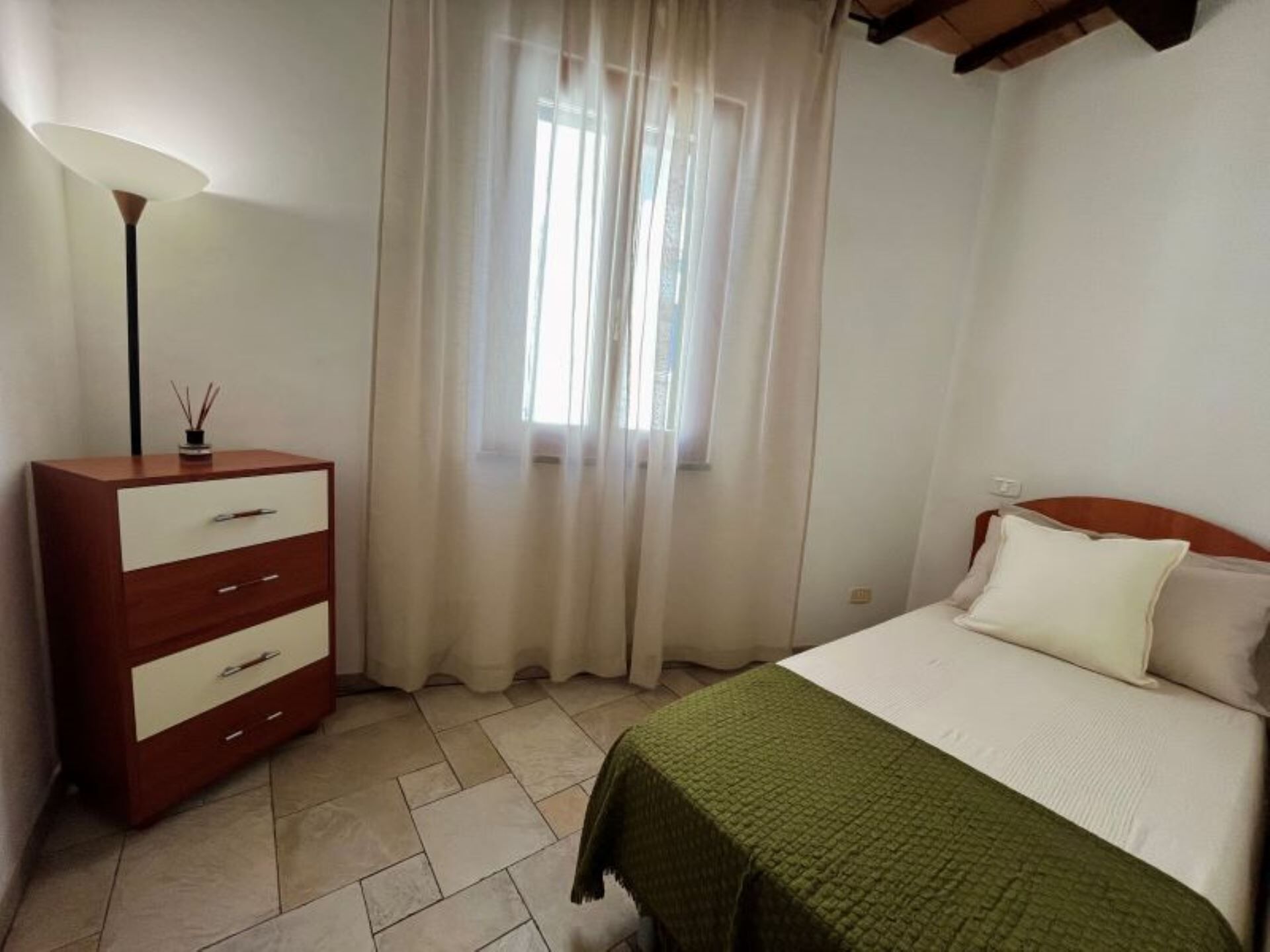 A bedroom with a bed, a dresser, a lamp, and a window with curtains.