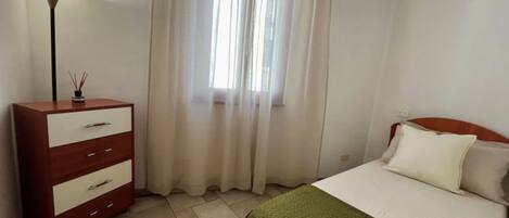 A bedroom with a bed, a dresser, a lamp, and a window with curtains.