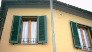 Un edificio con due finestre dotate di persiane verdi, una facciata gialla e un quadro elettrico a vista.