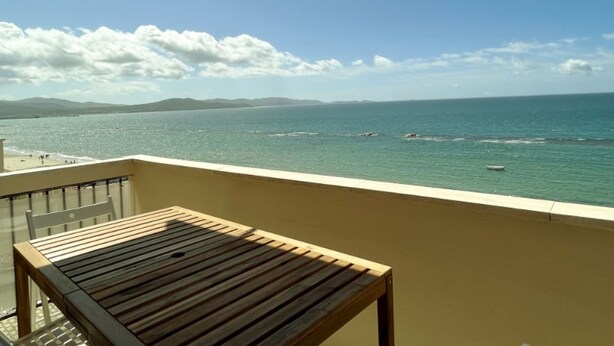 Un balcon avec une table en bois et une vue sur la mer et les montagnes lointaines.