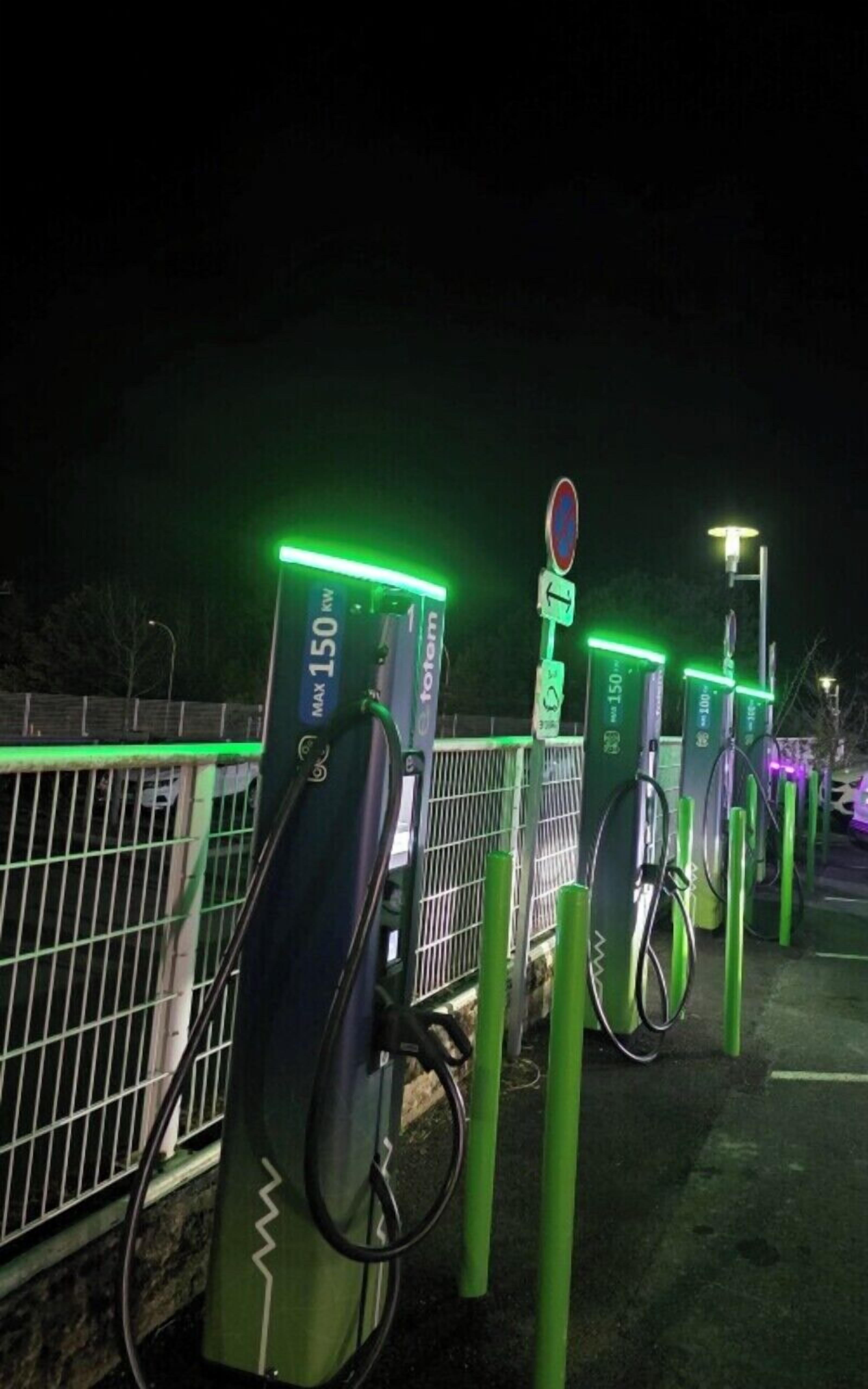 Fileira de estações de carregamento para veículos elétricos à noite, com iluminação verde.