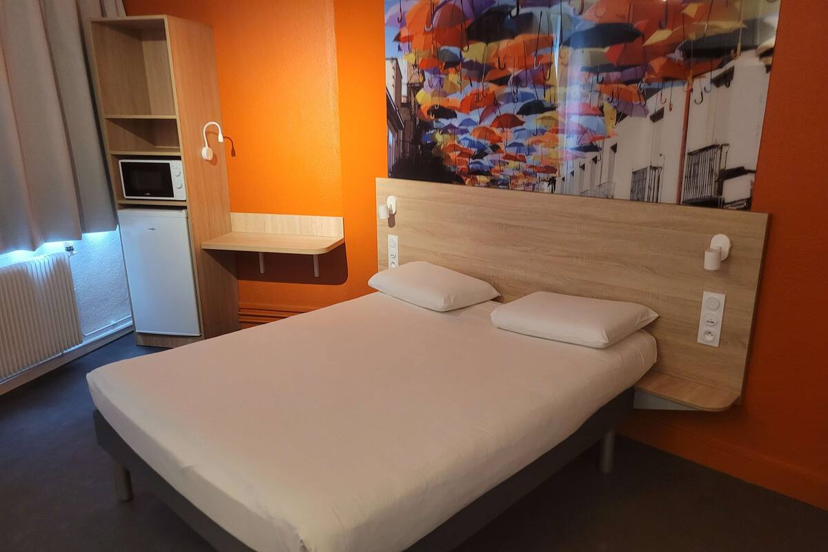 A hotel room with a bed, a small desk, a microwave, and a refrigerator.