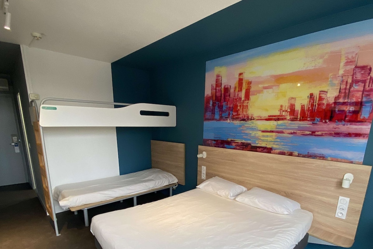 A hotel room with a bunk bed, a single bed, and a cityscape painting on the wall.