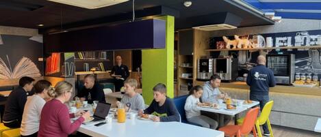 A modern dining area with tables and chairs, a counter with food items, and a visible security camera.