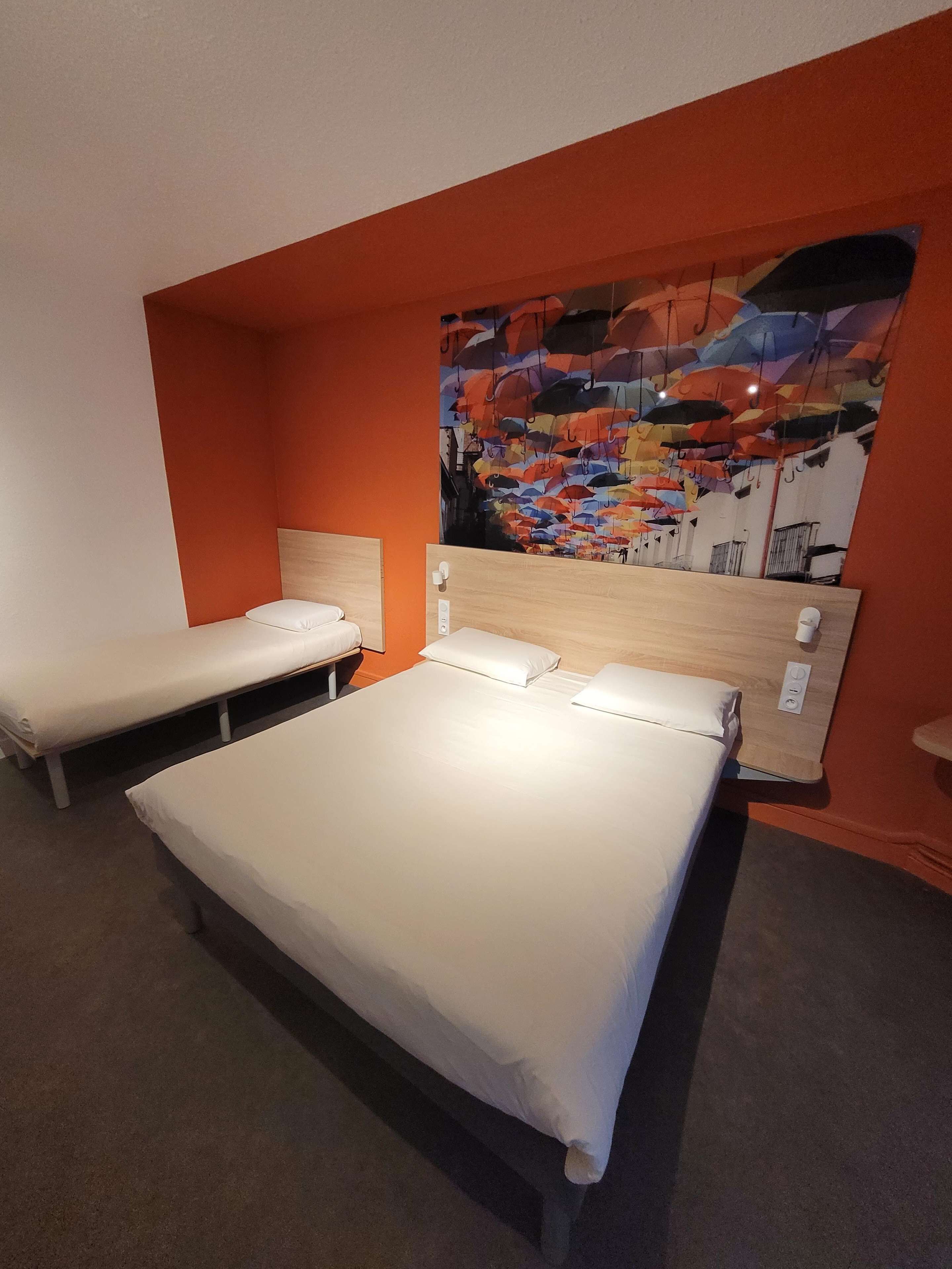 A hotel room with two single beds, a wooden headboard, and a colorful abstract mural on the wall.