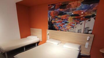 Una habitación de hotel con dos camas individuales, un cabecero de madera y un mural abstracto y colorido en la pared.