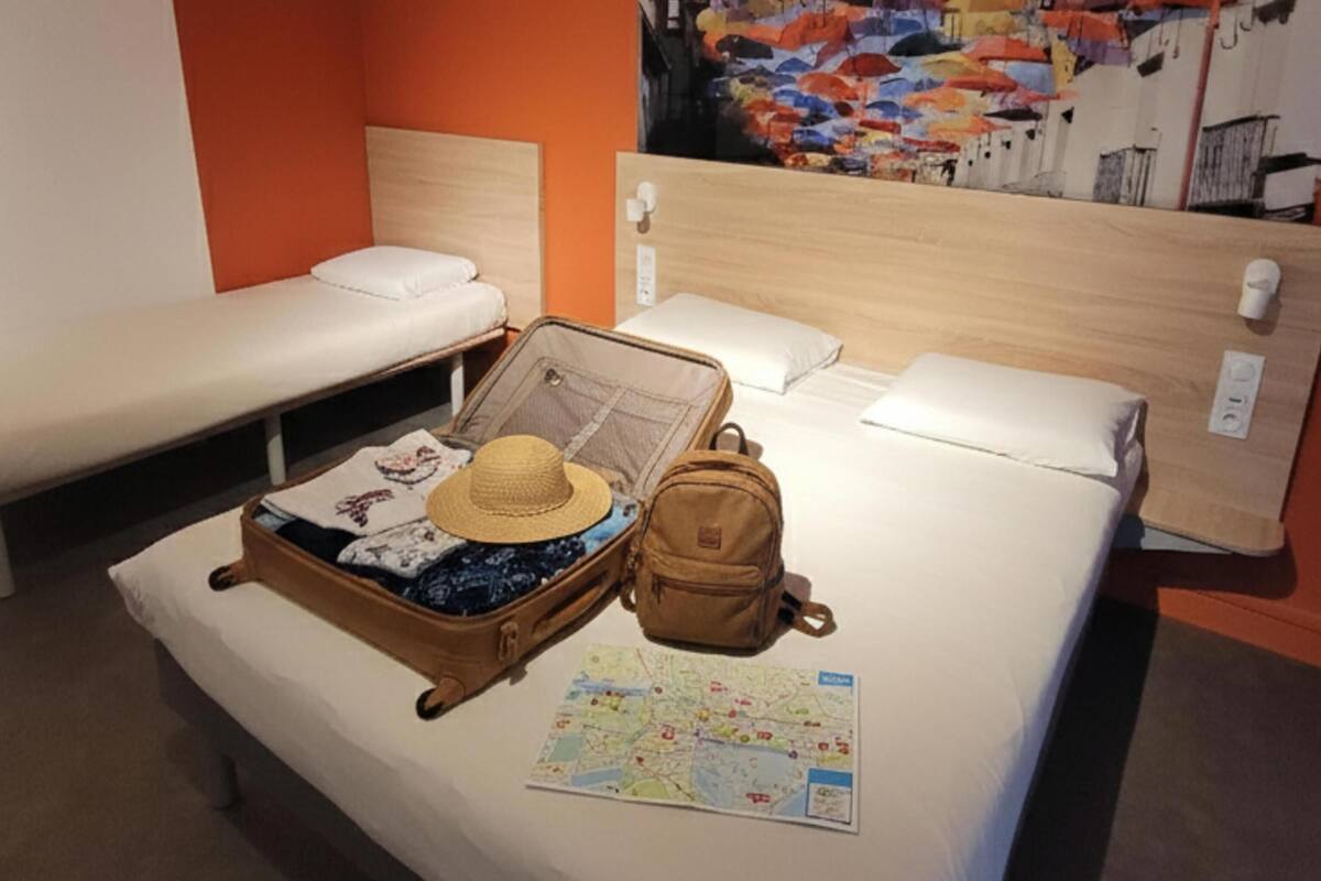 A hotel room with two single beds, a large bed with a suitcase, a map, and a hat on the bed.