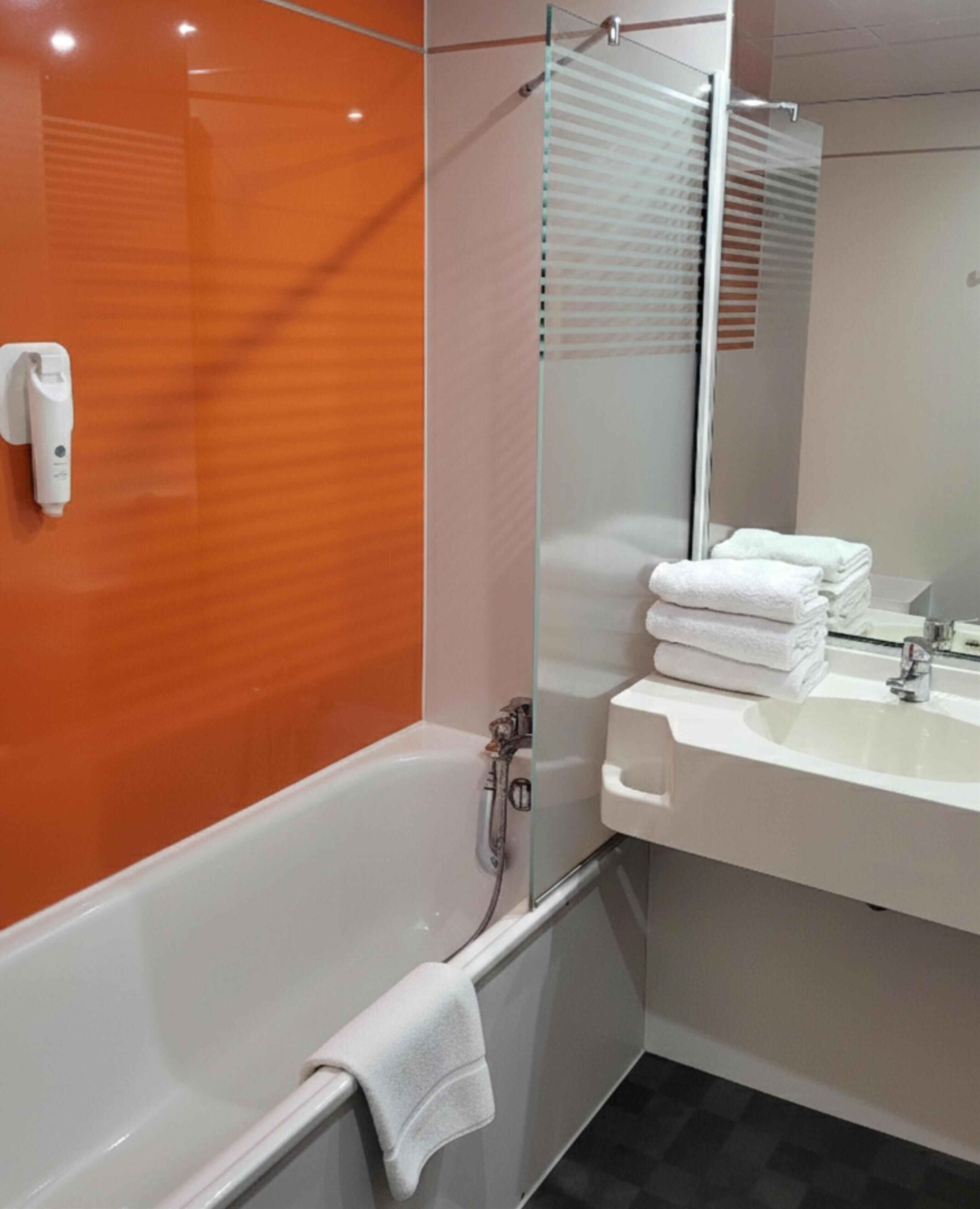 A modern bathroom with a glass shower enclosure, a white bathtub, and a sink with stacked white towels.