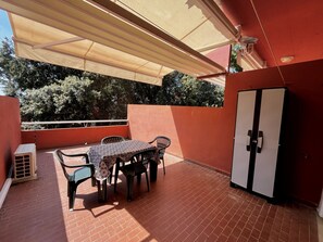 Une terrasse avec une table et des chaises, un meuble de rangement et une vue sur les arbres.