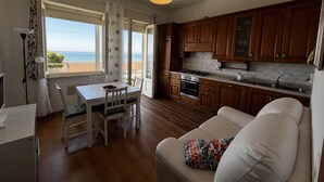 A compact kitchen with wooden cabinets, a dining table with chairs, and a sofa. - SPIAGGIA DI LEVANTE - ELBA (Follonica)