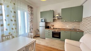 A compact kitchen with a microwave, oven, and sink, green cabinets, and a dining area with a table and chairs. - SPIAGGIA DI LEVANTE - ELBA (Follonica)