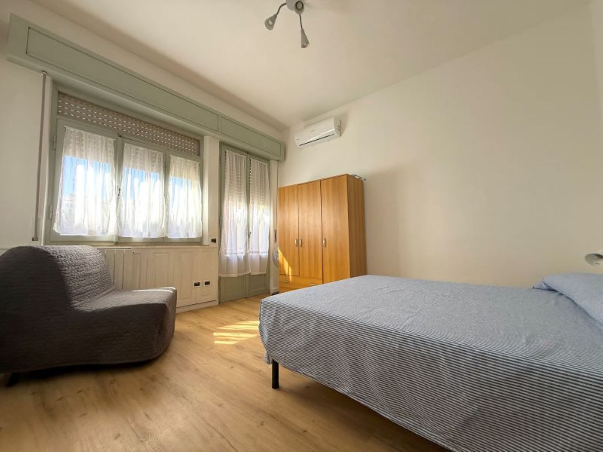 Une chambre à coucher avec un lit, une chaise, une armoire et une fenêtre avec des rideaux.