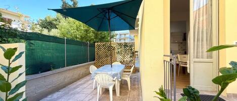Un patio exterior con mesa y sillas, una sombrilla verde y vistas del entorno.