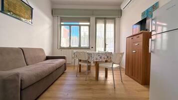 Un ambiente compatto con divano, tavolo da pranzo, sedie e frigorifero.