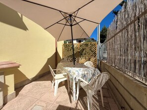 Eine Terrasse im Freien mit Tisch und Stühlen, einem beigen Sonnenschirm und einem Holzzaun.