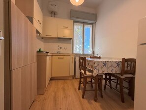 Eine kleine Küche mit Holzausstattung, einem Esstisch mit Stühlen und einem Fenster, das für natürliches Licht sorgt.