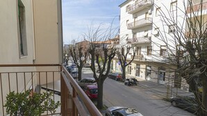 Ein Balkon mit einem Blumentopf, Blick auf eine Straße mit parkenden Autos und ein Gebäude mit Balkonen.