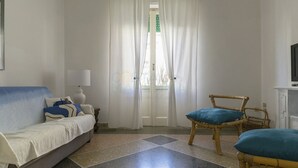 Ein Zimmer mit einer Couch, einem Sessel, einer Lampe und einem Fernseher.